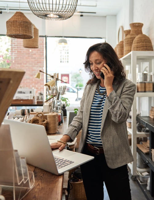 a small business owner uses a computer and talks on a telephone in her home decor shop